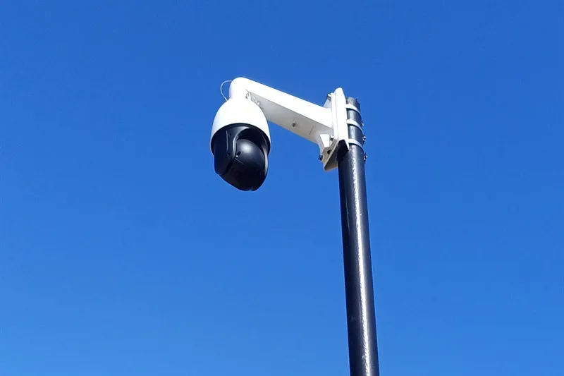 Pan-tilt-zoom security camera on a steel pole against a blue sky
