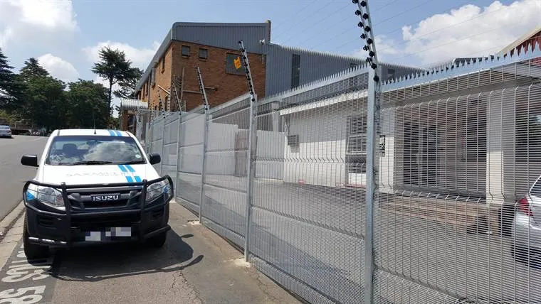 Galvanised clear view mesh fence with electric fence strands on top along a business frontage, a Saxmoore bakkie parked in front