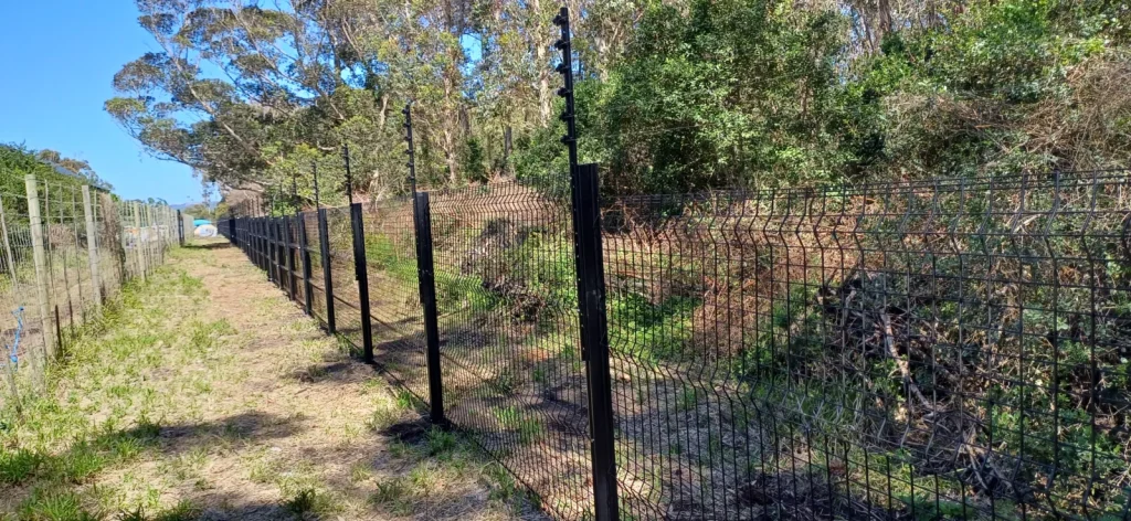 Long run of black clearview fencing with electric strands on top beside a grass track, coastal estate, Plettenberg Bay