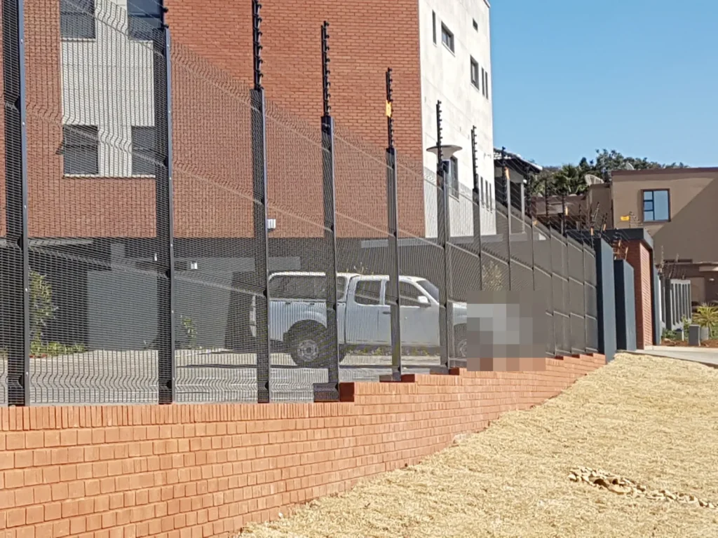 Black clearview fence with an electric fence on top, on a face-brick dwarf wall along a commercial front boundary