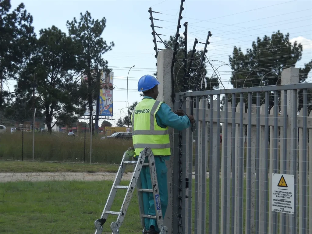 Installer in PPE on a ladder working on the electric strands above a palisade fence