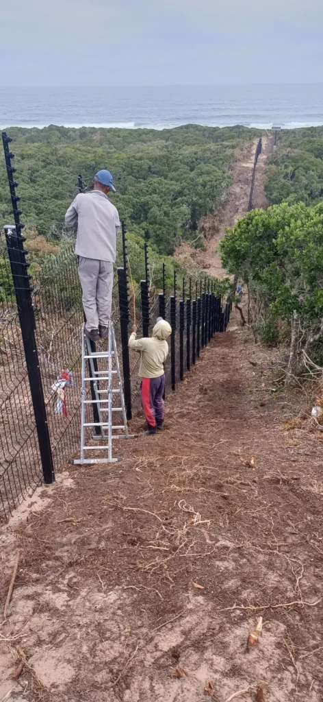 Two Saxmoore installers wiring the top strands of an electric fence on a clearview fence, coastal estate, Plettenberg Bay
